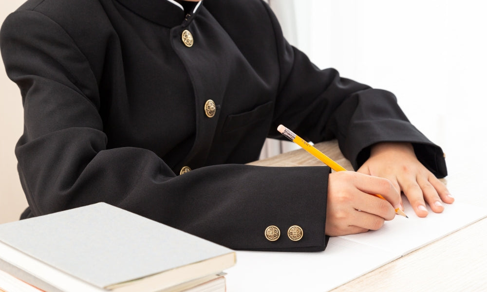 Japanese student in a black stand-collar gakuran school uniform writing at a desk