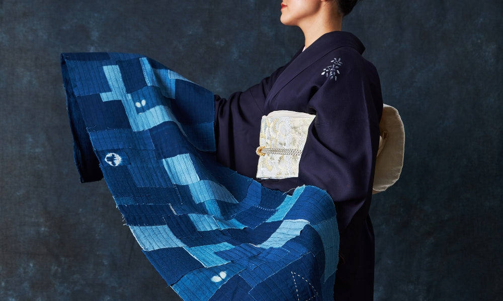Japanese boro patchwork textile in indigo cotton with visible sashiko running stitches, worn by a model in dark kimono