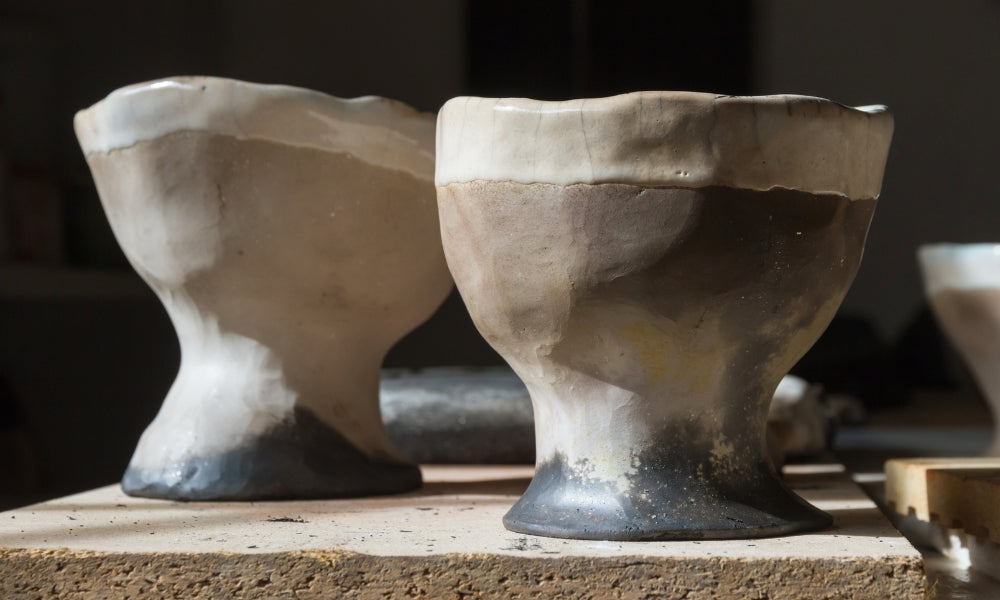 Two Japanese raku pottery tea bowls (chawan) with hand-formed shapes and dark-to-light glaze tones, on a workshop surface