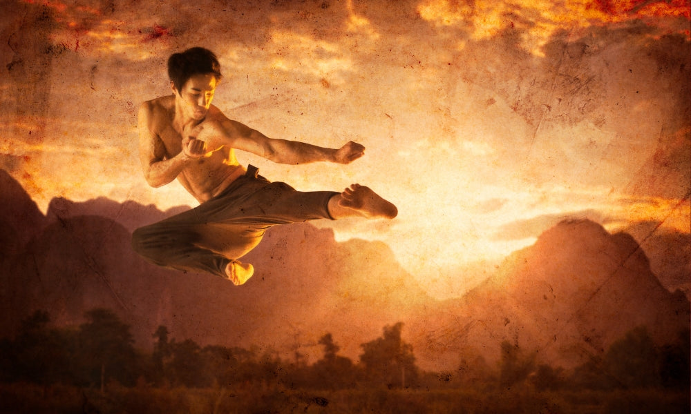 A bare-chested martial artist performing a dynamic flying kick against a fiery sunset over mountains, evoking the legendary image of the ninja warrior