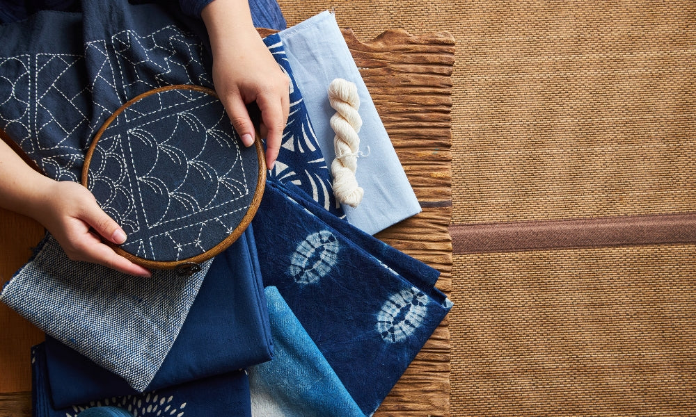 Traditional Japanese sashiko embroidery on indigo fabric with hoop, thread skein, and patterned cloth - sashiko stitching