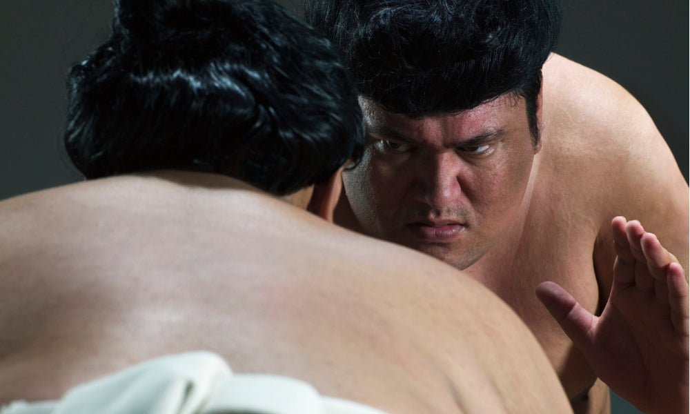 Two sumo wrestlers with traditional topknots facing off at close range in intense concentration before a bout