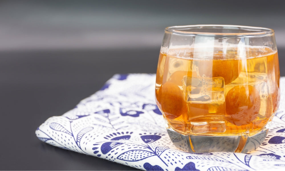 Glass of umeshu, the Japanese plum wine, served on the rocks with whole ume fruits at the bottom