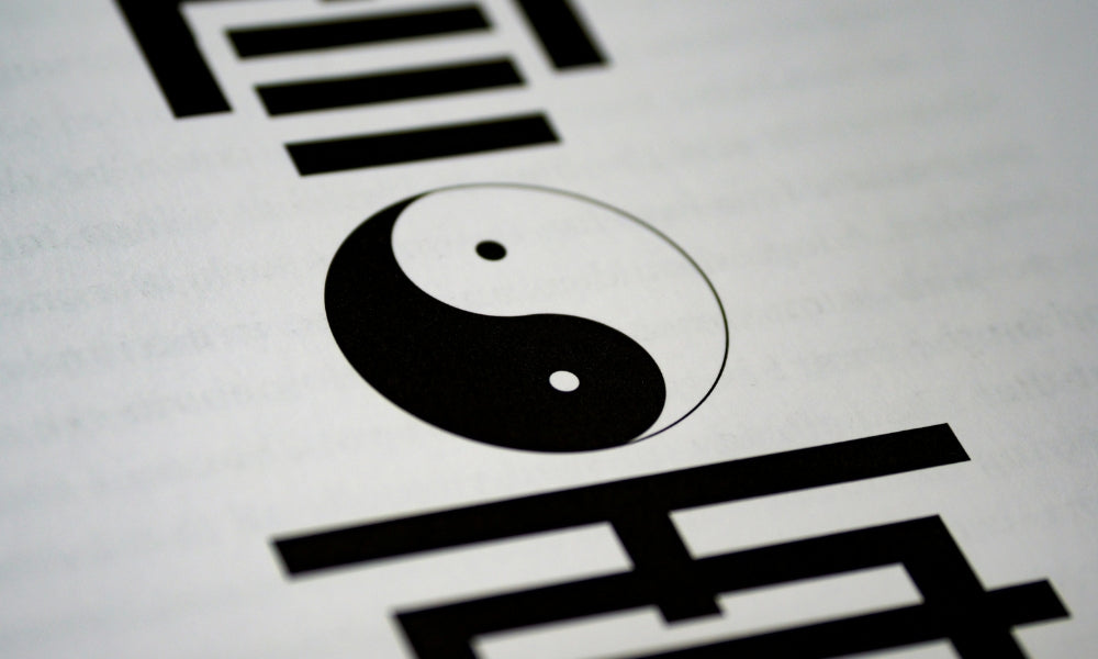 The black and white yin and yang symbol (taijitu) printed on a page surrounded by I Ching trigram lines, representing the philosophy of complementary opposites