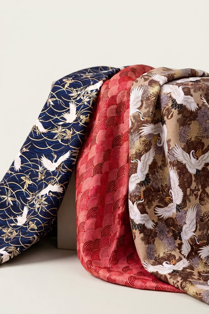 Furoshiki collection: three Japanese wrapping cloths draped side by side, printed with flying cranes on navy, red seigaiha waves and chrysanthemums