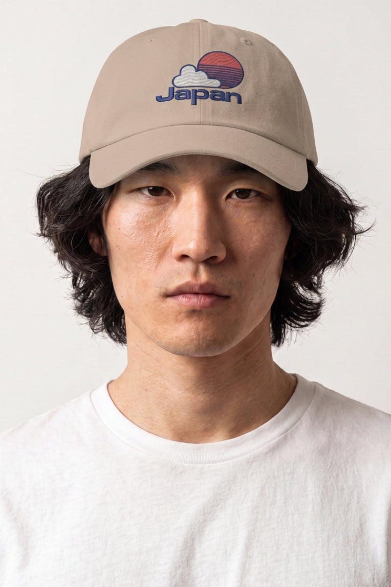 Japanese caps collection: man wearing a beige baseball cap embroidered with a rising sun, cloud and Japan lettering in navy and red
