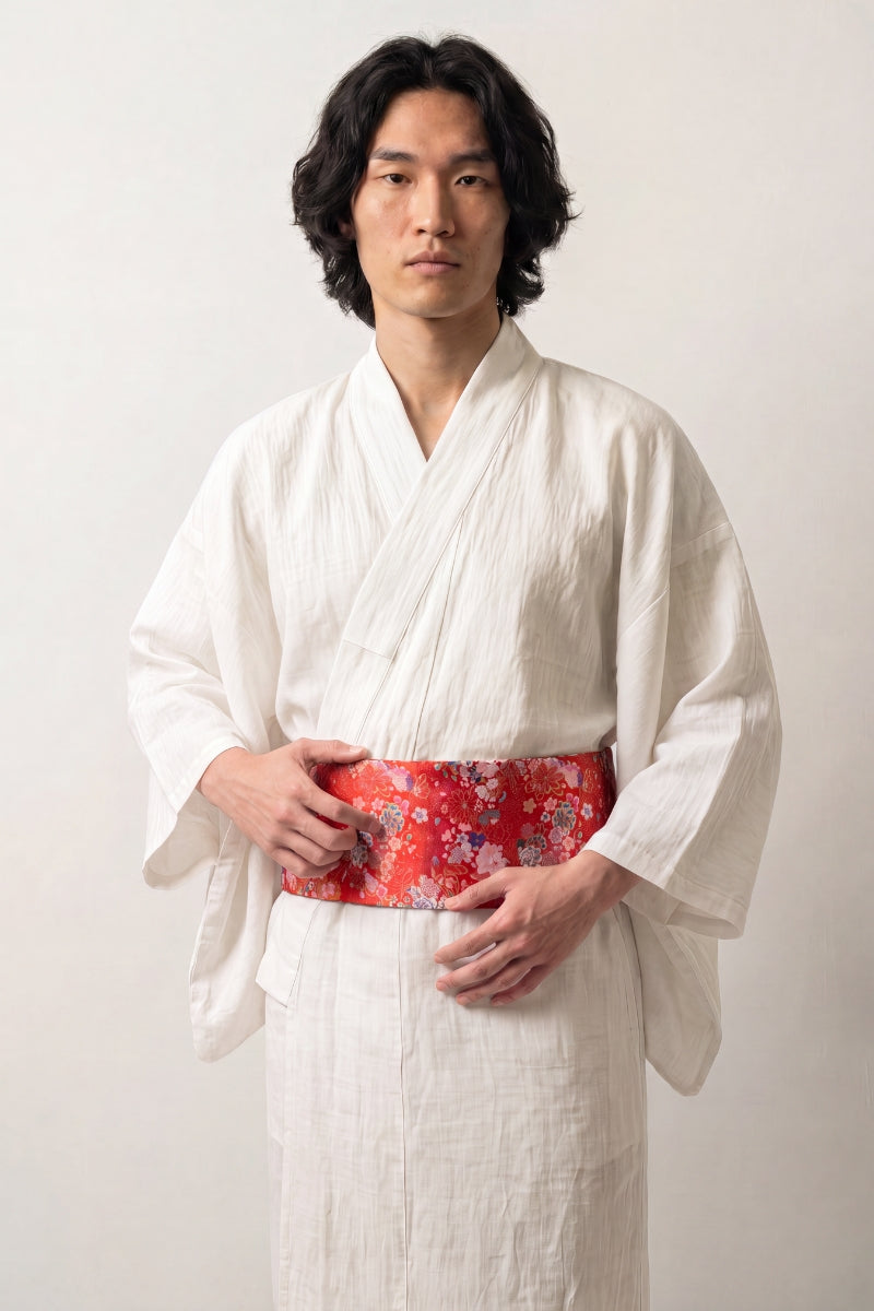 Obi belt collection: man in a white linen kimono wearing a red brocade obi belt woven with pink, white and blue blossoms