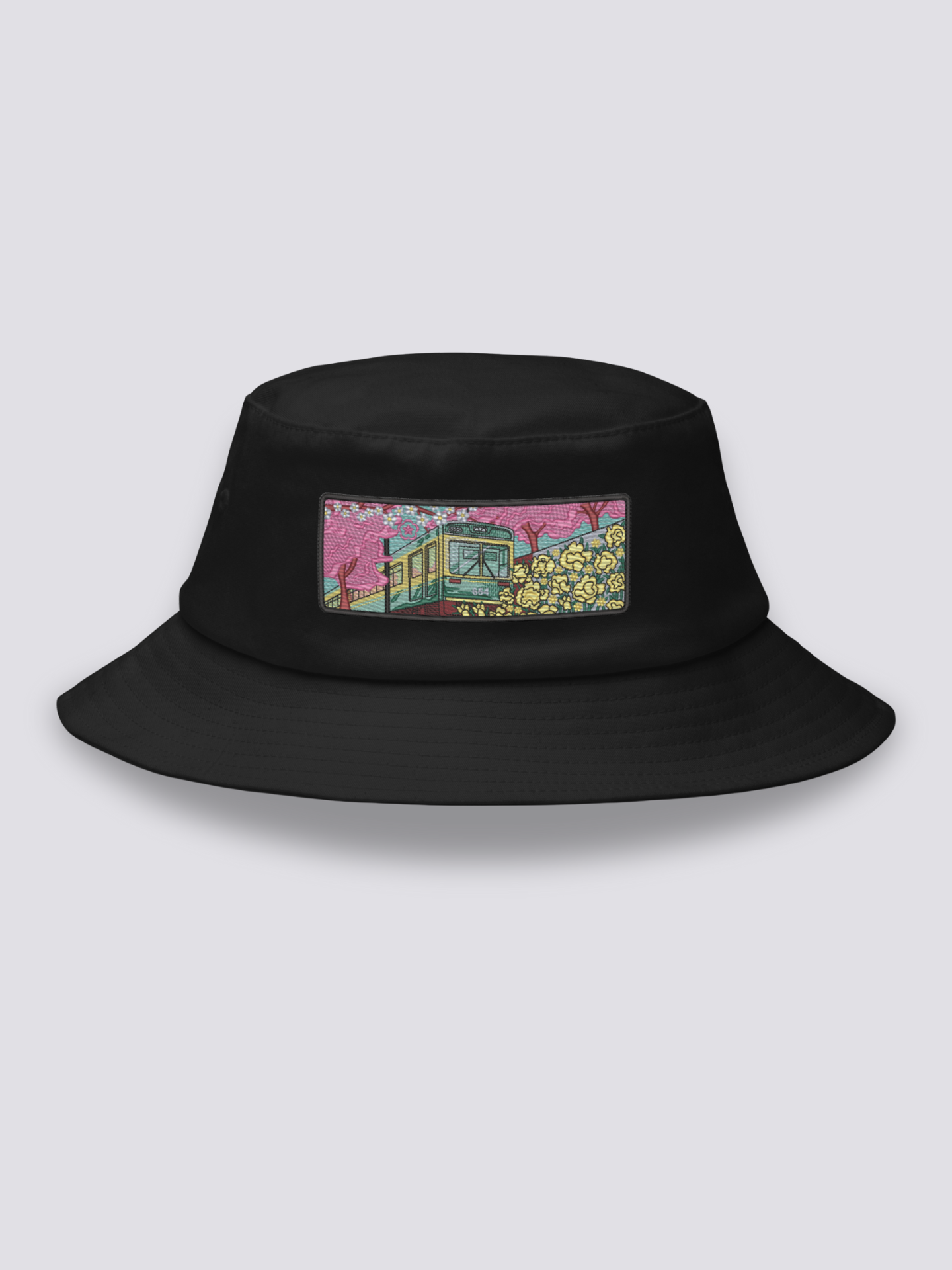 Black bucket hat with an embroidered patch of a small vintage green and yellow train crossing cherry blossom and yellow flower fields