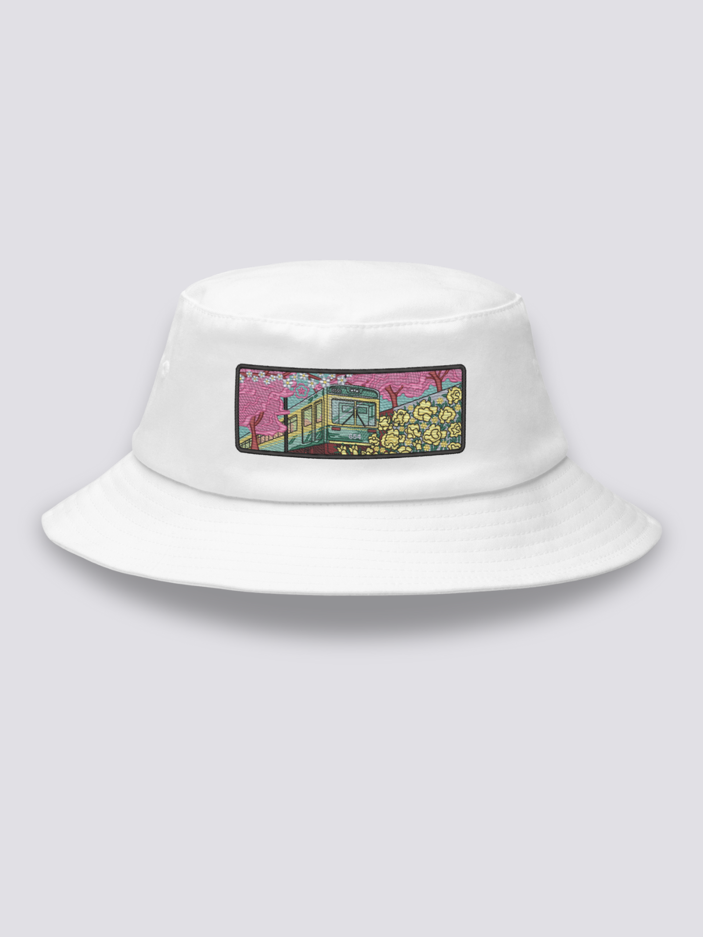 Khaki bucket hat with an embroidered patch of a small vintage green and yellow train crossing cherry blossom and yellow flower fields