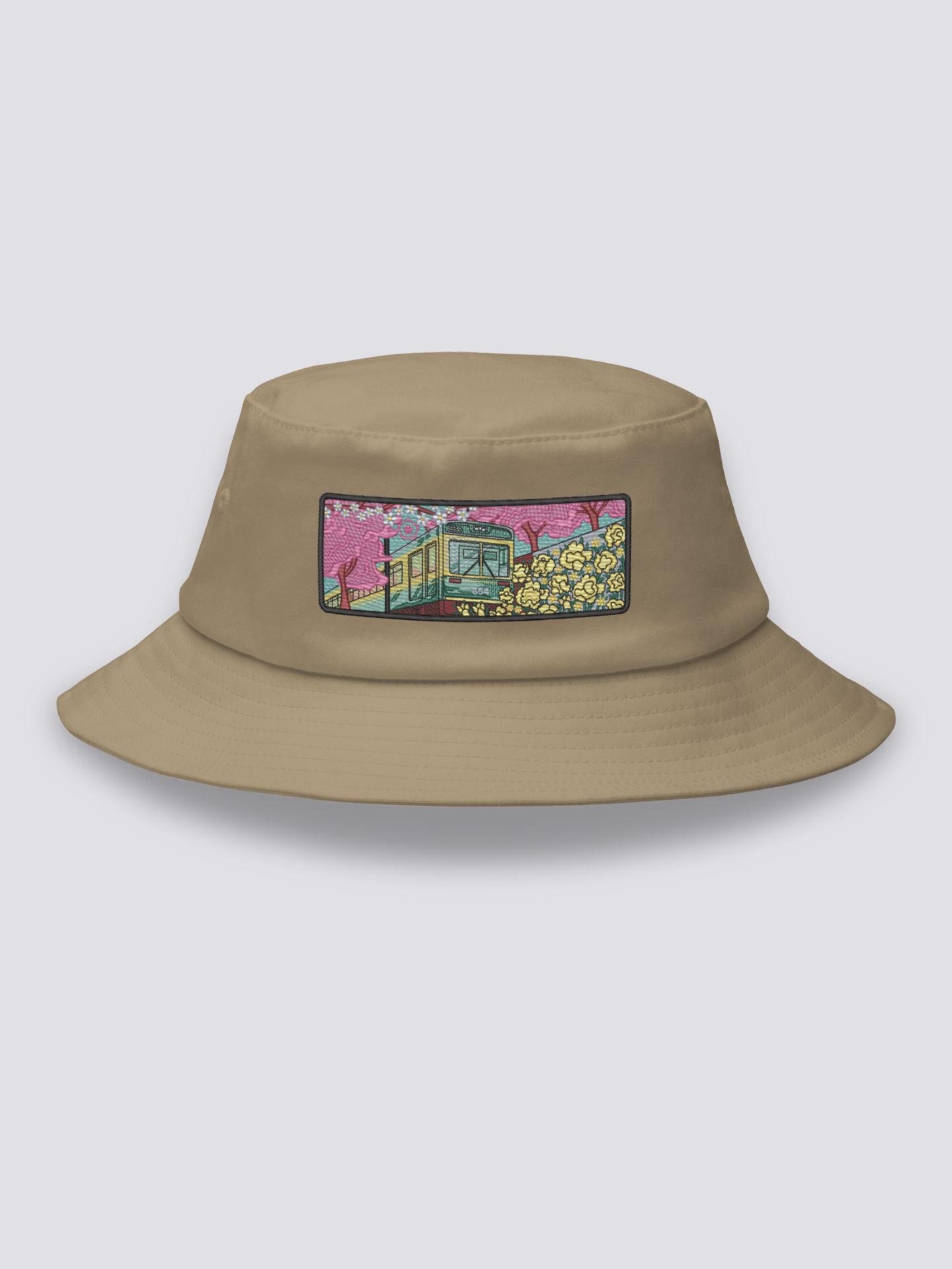 White bucket hat with an embroidered patch of a small vintage green and yellow train crossing cherry blossom and yellow flower fields