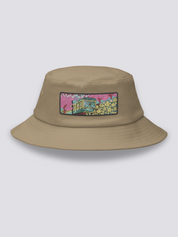 White bucket hat with an embroidered patch of a small vintage green and yellow train crossing cherry blossom and yellow flower fields