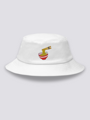 White bucket hat with an embroidered steaming ramen bowl, noodles lifted on chopsticks and pink narutomaki