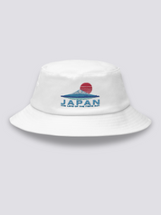 White bucket hat with an embroidered striped red sun above a deep blue Mount Fuji and JAPAN lettering in navy