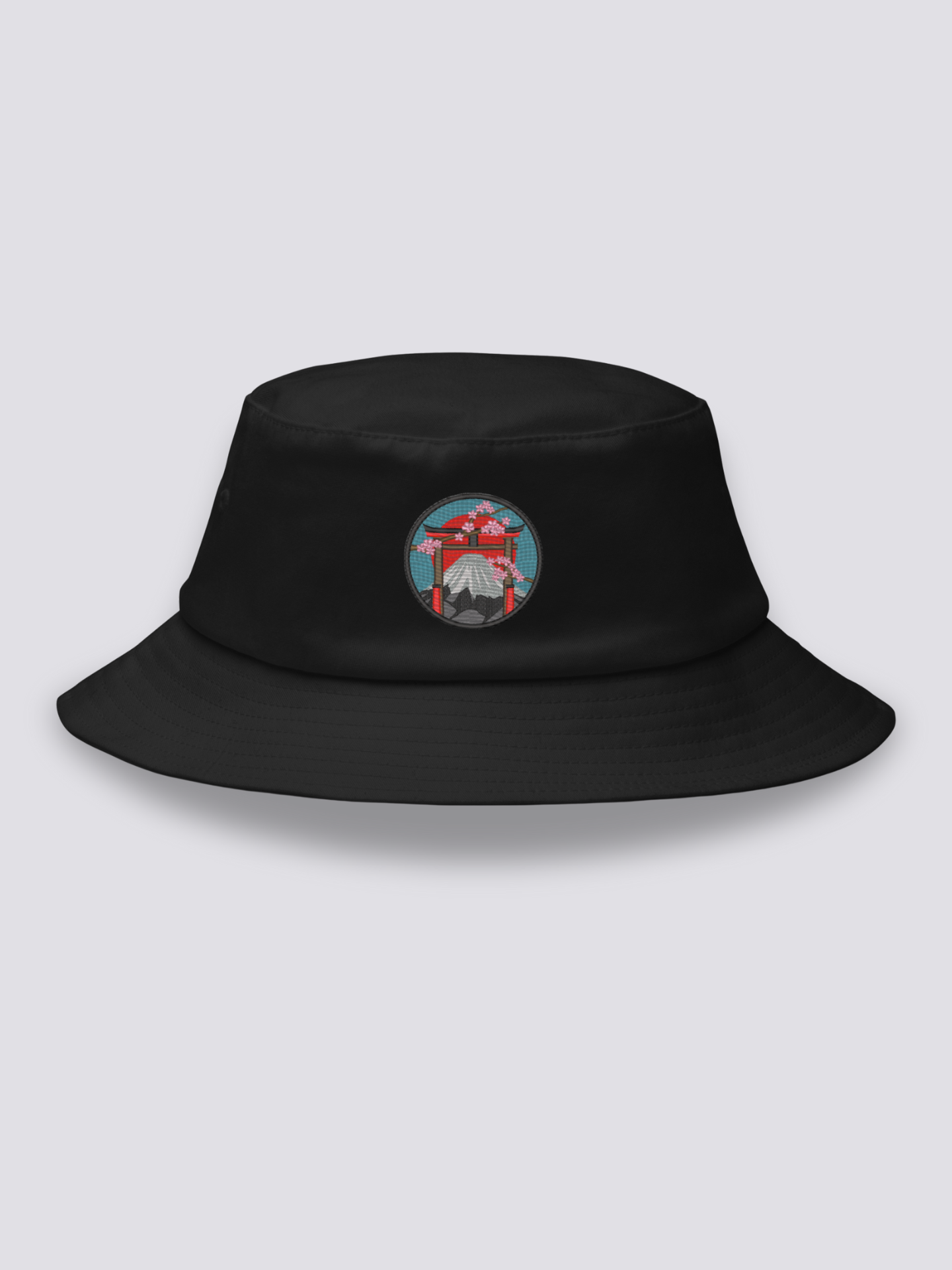 Black bucket hat with an embroidered medallion of a vermilion torii before Mount Fuji, framed by cherry blossom under a red sun
