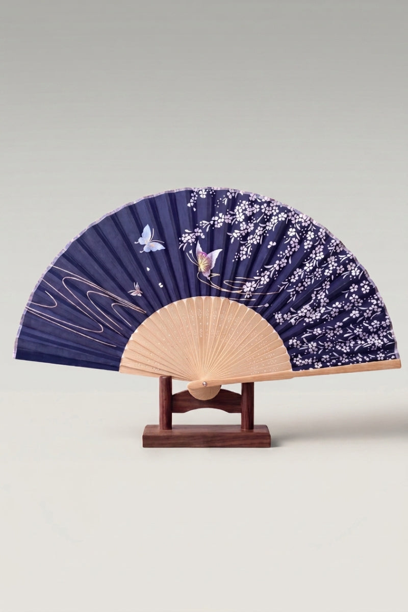 Japanese folding fan 'Ebino' — white cherry blossom and butterflies on a deep navy folding fan, shown open on a wooden stand