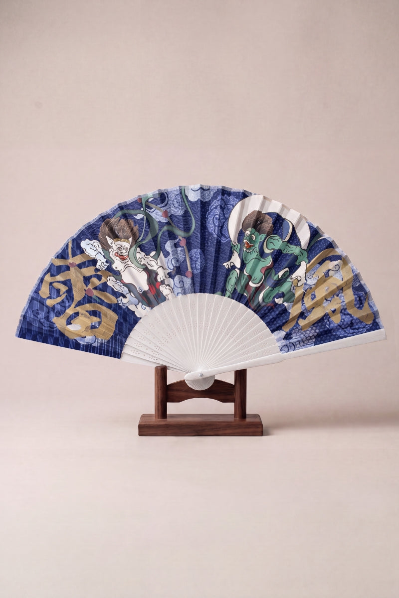 Japanese folding fan with the wind god Fujin and thunder god Raijin in gold on a deep indigo leaf