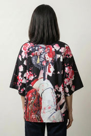 Back view of the black Sakura x Geiko kimono: a geisha in full dress standing among falling cherry blossom