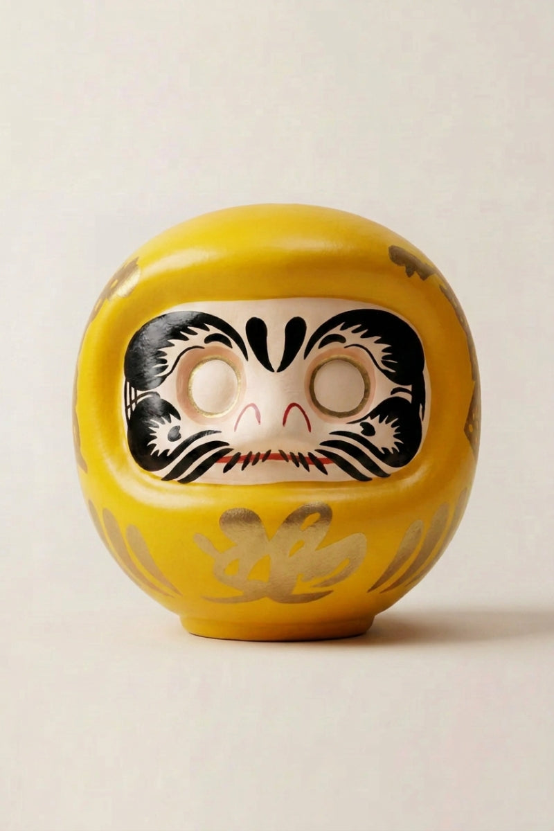 Golden-yellow daruma doll with gold calligraphy and blank white eyes, traditional Japanese good-luck charm