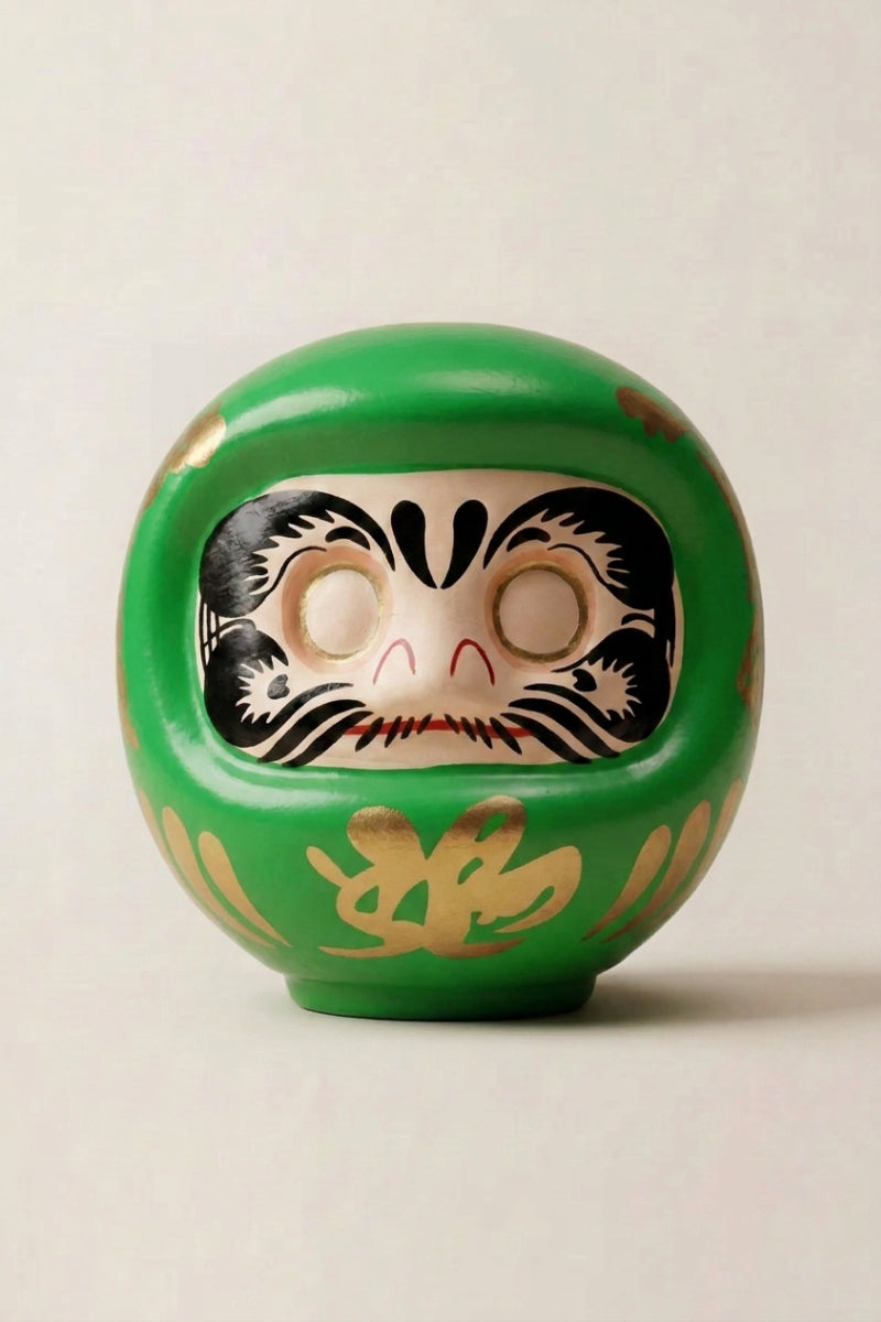 Green daruma doll with gold calligraphy and blank white eyes, traditional Japanese good-luck charm for goals