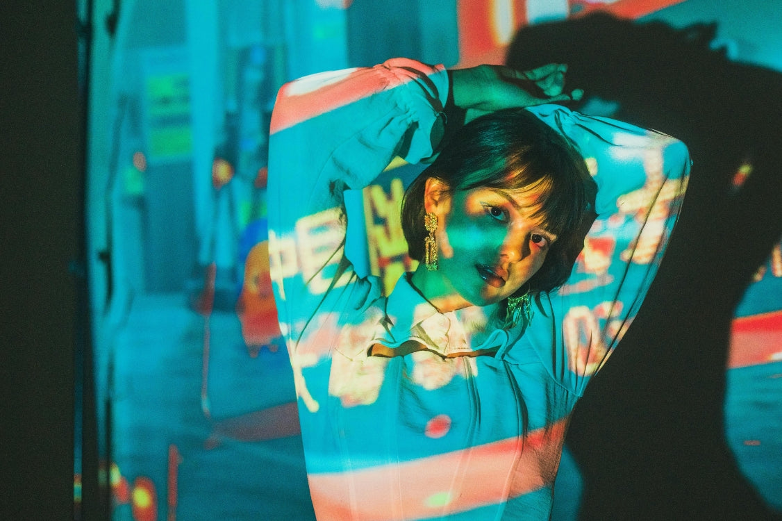 Asian model posing under neon projection art, wearing modern streetwear for Japan Clothing.