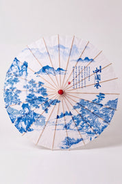 Traditional Japanese paper umbrella with a blue mountain landscape with pines and houses on a white canopy, shown open on bamboo ribs