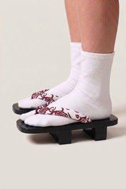 Japanese Geta 'Aomori' — black wooden platform sandals with deep-red burgundy straps and white floral motif, traditional two-tooth geta worn with white socks