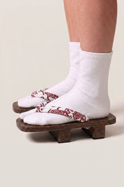 Japanese Geta 'Shakori' — wooden platform sandals with deep-red burgundy hanao straps in a white floral print, traditional geta worn with white tabi socks