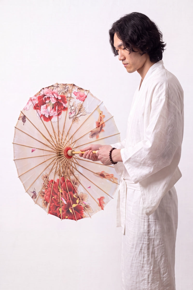 Traditional Japanese paper umbrella with red and pink peonies, butterflies and swimming koi on a cream canopy, held open overhead by a model in a white kimono