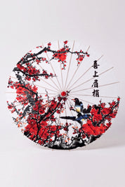 Traditional Japanese paper umbrella with an ink-brushed plum tree with red blossom and small birds on a white canopy, shown open on bamboo ribs