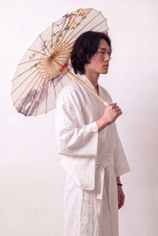 Traditional Japanese paper umbrella with a flowering branch, a pink lotus and a misty stone bridge on an off-white ground, held open overhead by a model in a white kimono