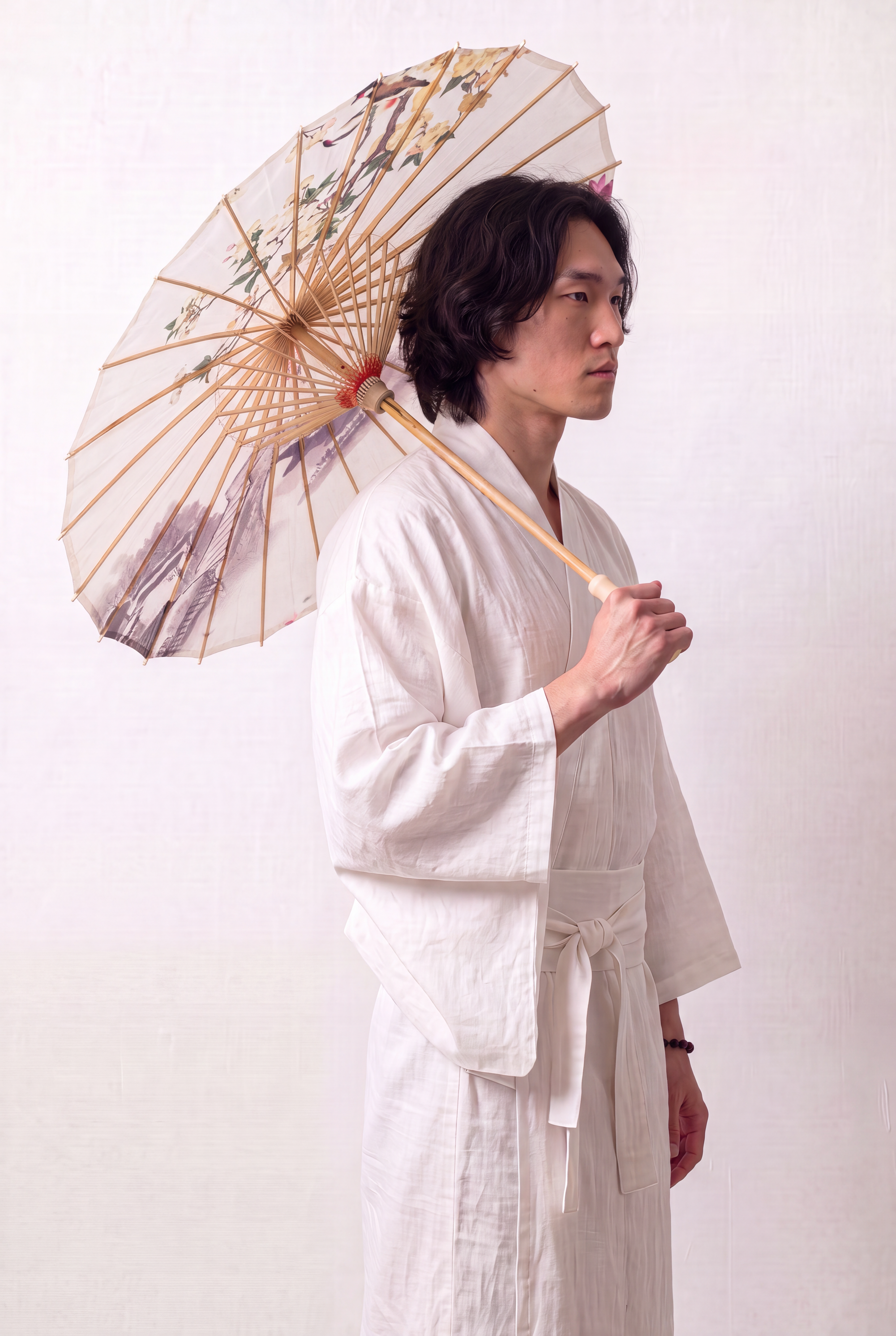 Traditional Japanese paper umbrella with a flowering branch, a pink lotus and a misty stone bridge on an off-white ground, held open overhead by a model in a white kimono