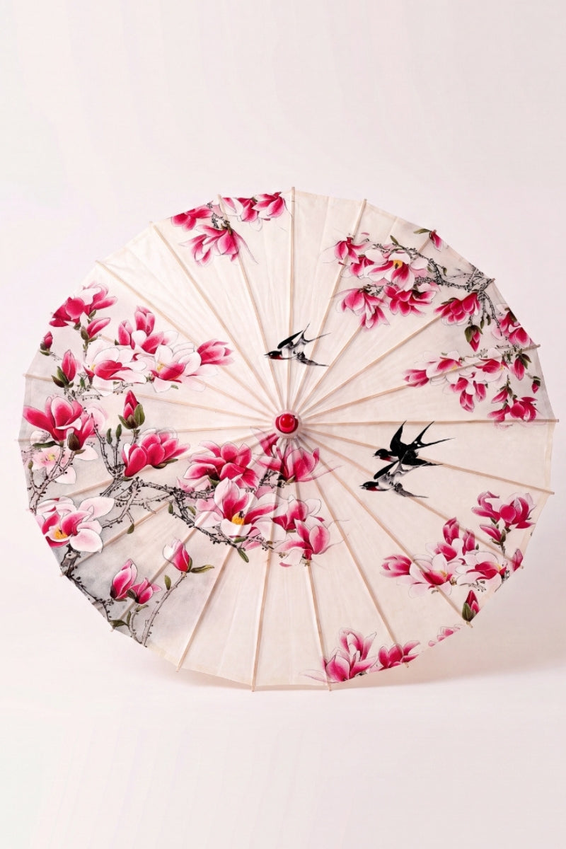Traditional Japanese paper umbrella with a ring of pink magnolias and black swallows on a warm ivory canopy, shown open on bamboo ribs