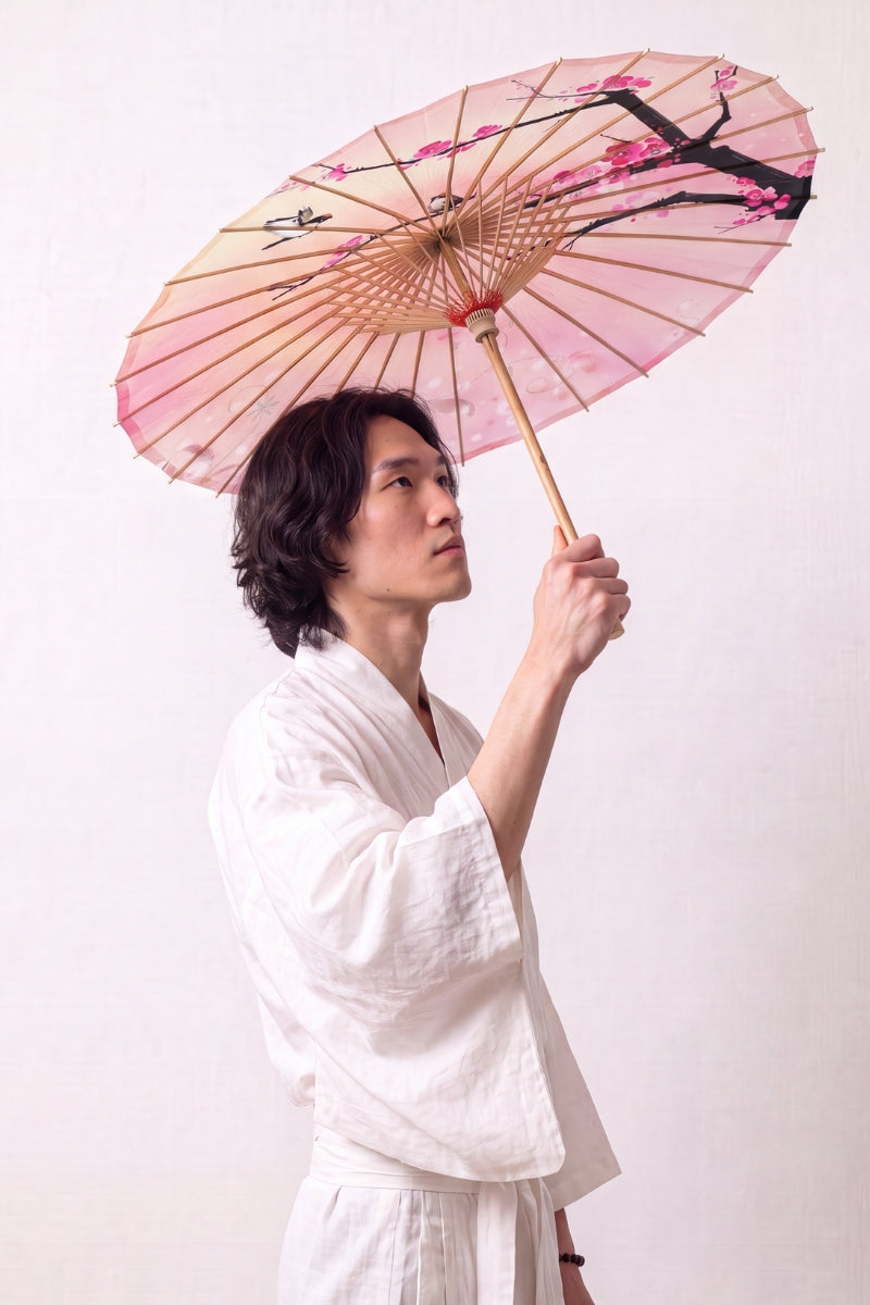 Traditional Japanese paper umbrella with pink cherry blossom on a peach-and-pink ground, held open by a model in a white kimono