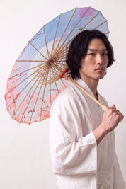 Traditional Japanese paper umbrella with pink blossom scattered across a pale sky-blue ground, held open by a model in a white kimono