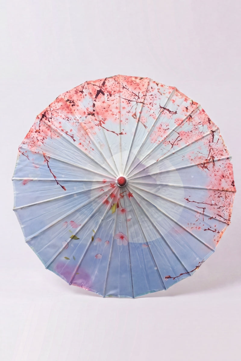 Traditional Japanese paper umbrella with pink cherry blossom raining from above on a sky-blue canopy fading to white, shown open on bamboo ribs