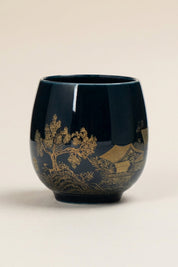 Handleless Japanese yunomi tea cup in dark navy-black glaze, decorated with a gold temple pavilion among pine trees