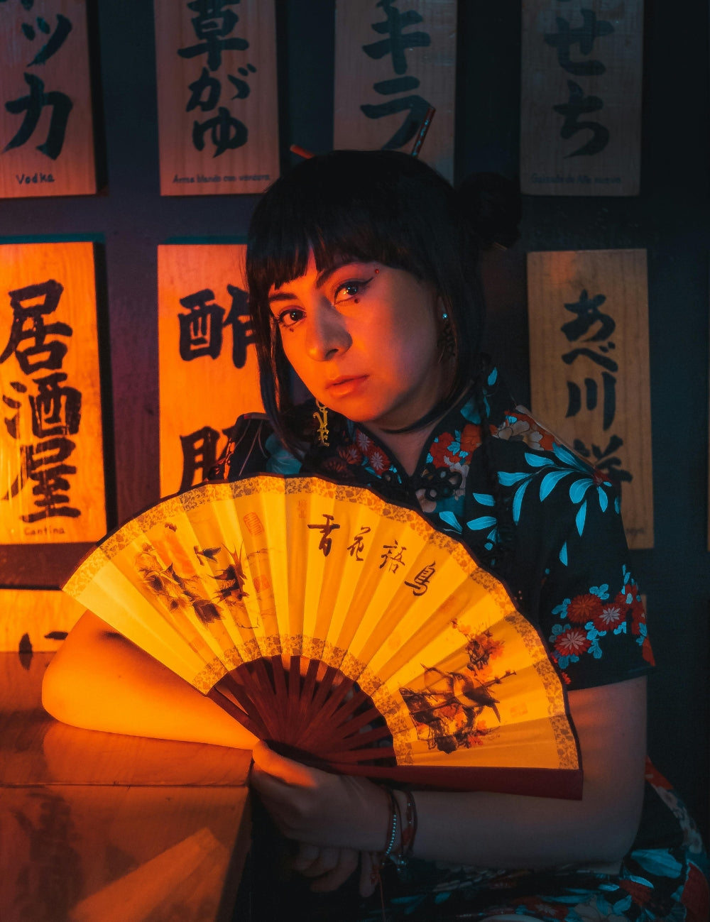 Woman wearing a Japanese-style dress holding a traditional hand fan under warm Tokyo lights — part of the Japanese Dresses collection by Japanstreet.