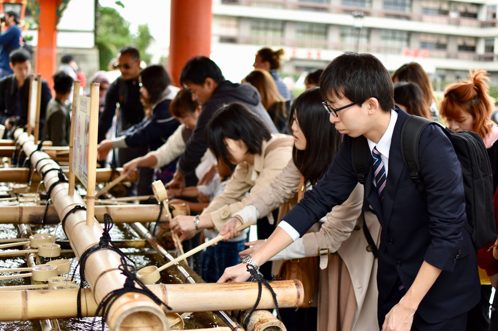Visitors at a Kyoto temple performing traditional water purification — part of the Japan Clothing Lookbook showcasing Japanese culture and fashion inspiration.
