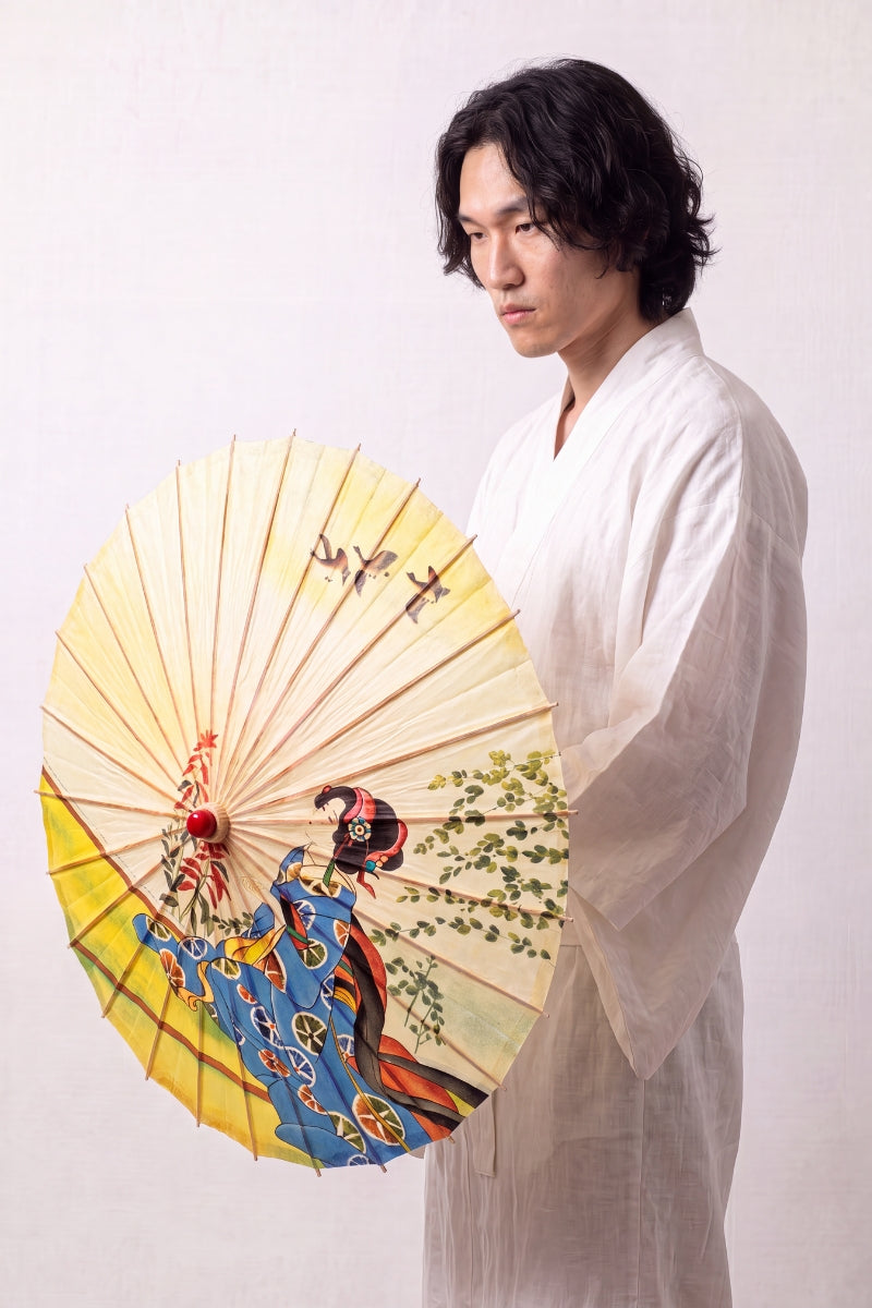 Traditional Japanese paper umbrella with a woman in a blue kimono kneeling under wild geese on a pale yellow ground, held open overhead by a model in a white kimono