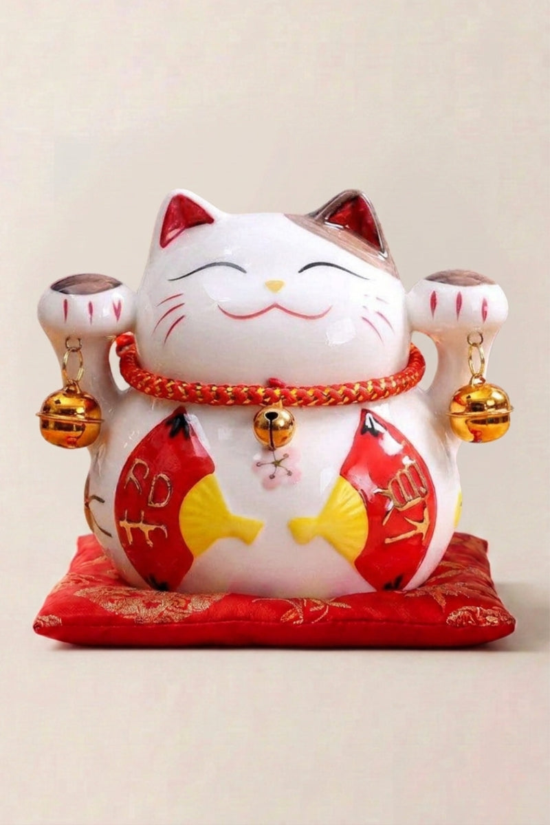 Maneki Neko Money box 'Fans' — Japanese maneki-neko lucky cat money box, white ceramic lucky cat with a red bib and gold bells holding a fish on a red cushion