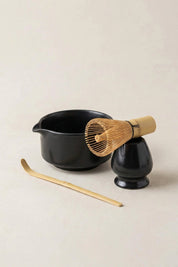 Japanese matcha set in black ceramic: spouted chawan bowl, whisk stand holding a bamboo chasen whisk, and a bamboo chashaku scoop