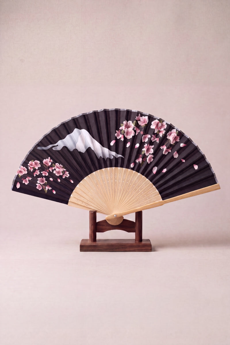 Japanese folding fan with Mount Fuji and pink cherry blossom on a black leaf, mounted on pale bamboo ribs