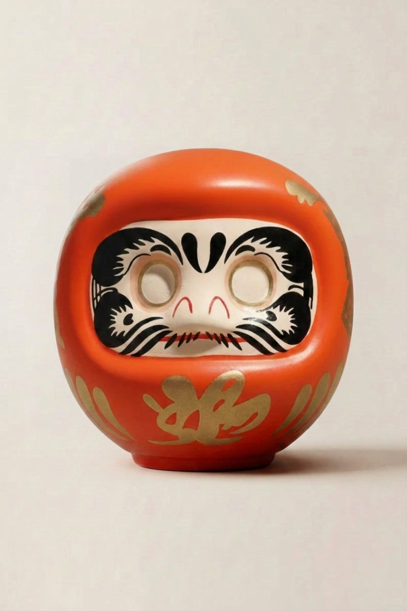 Orange daruma doll with gold calligraphy and blank white eyes, traditional Japanese good-luck charm