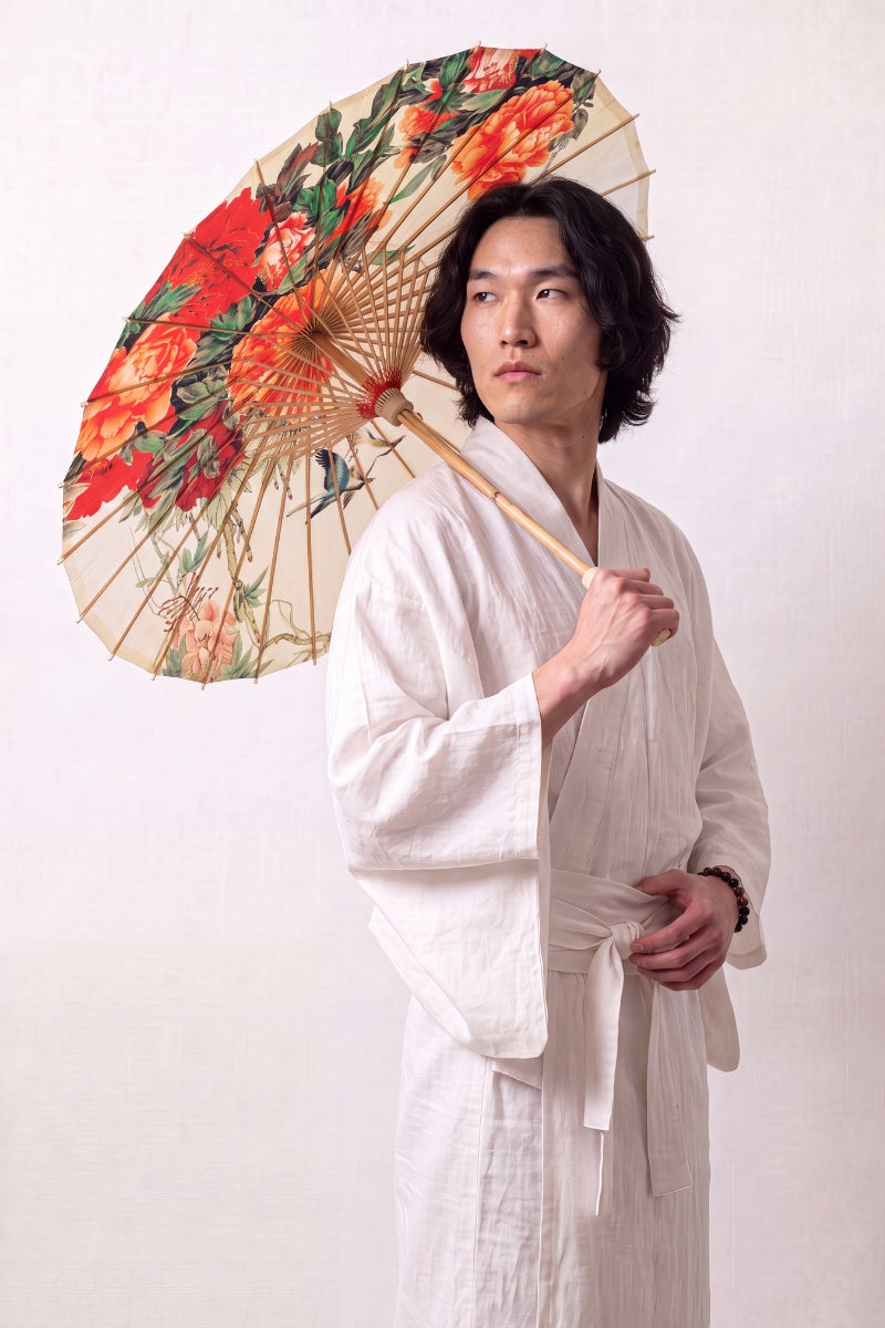 Traditional Japanese paper umbrella with orange and red peonies with a pair of birds on a cream-to-ivory ground, held open overhead by a model in a white kimono