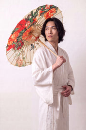 Traditional Japanese paper umbrella with orange and red peonies with a pair of birds on a cream-to-ivory ground, held open overhead by a model in a white kimono