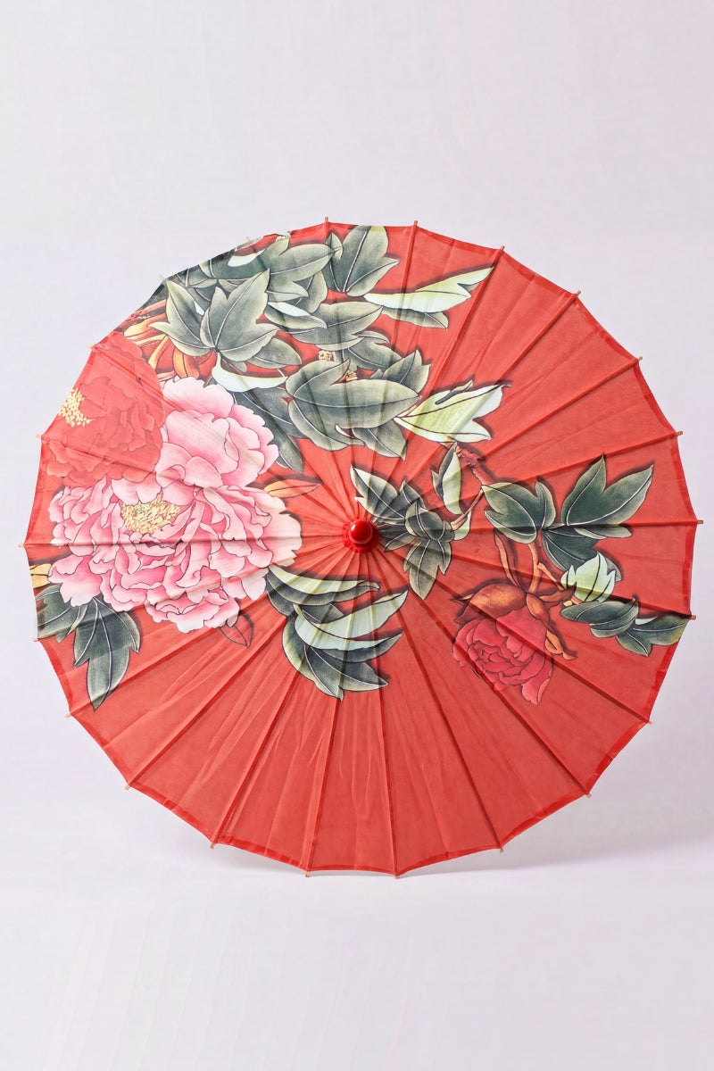 Traditional Japanese paper umbrella with large blush-pink peonies and green leaves on a bright red canopy, shown open on bamboo ribs