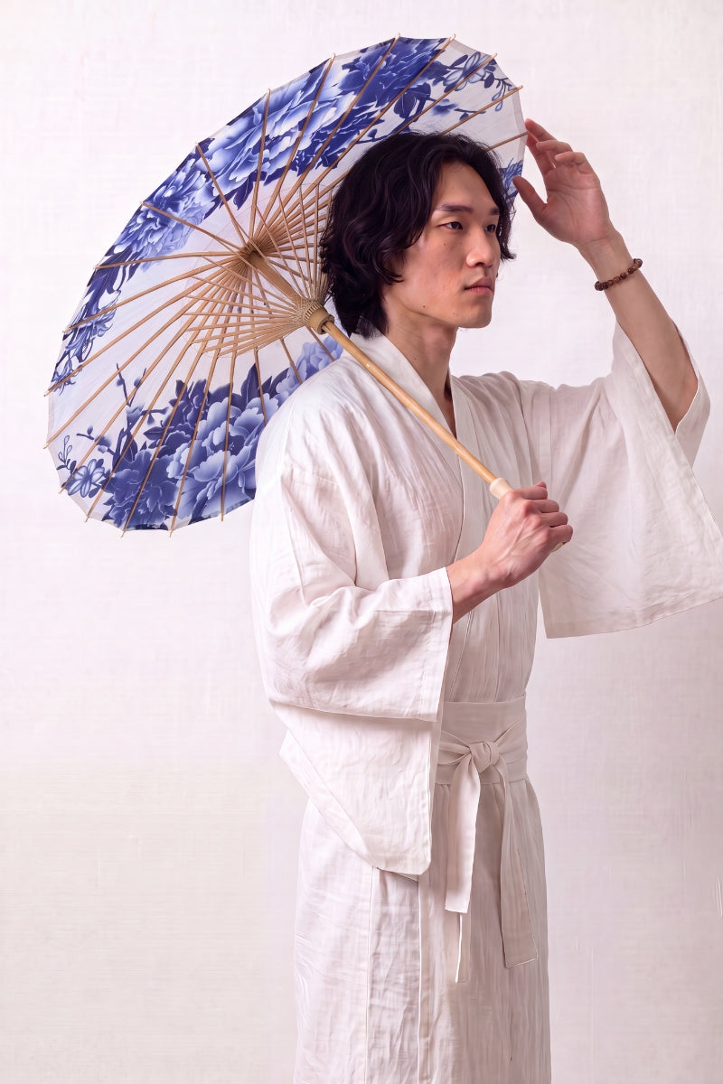Traditional Japanese paper umbrella with cobalt and pale blue peonies in porcelain style on a white canopy, held open overhead by a model in a white kimono