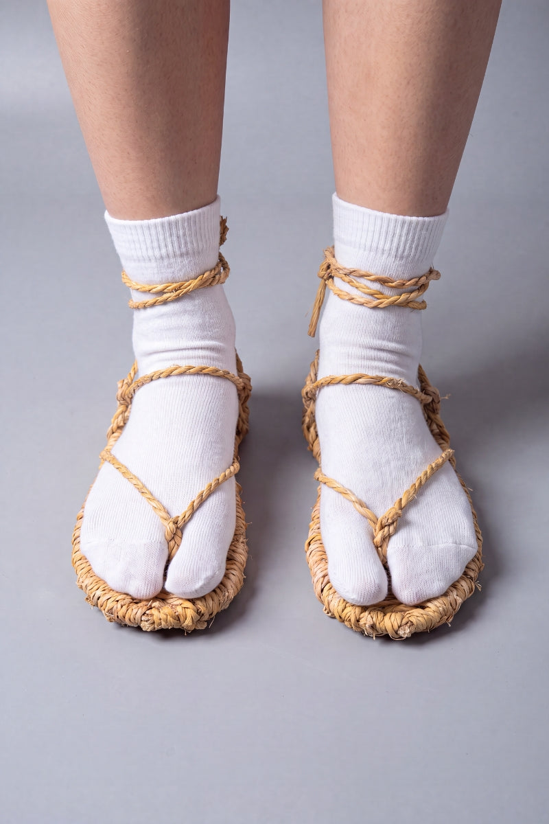 Waraji sandals worn over white tabi socks, front view: the split-toe sock sits under the straw thong and rope lacing