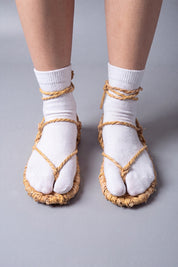 Waraji sandals worn over white tabi socks, front view: the split-toe sock sits under the straw thong and rope lacing
