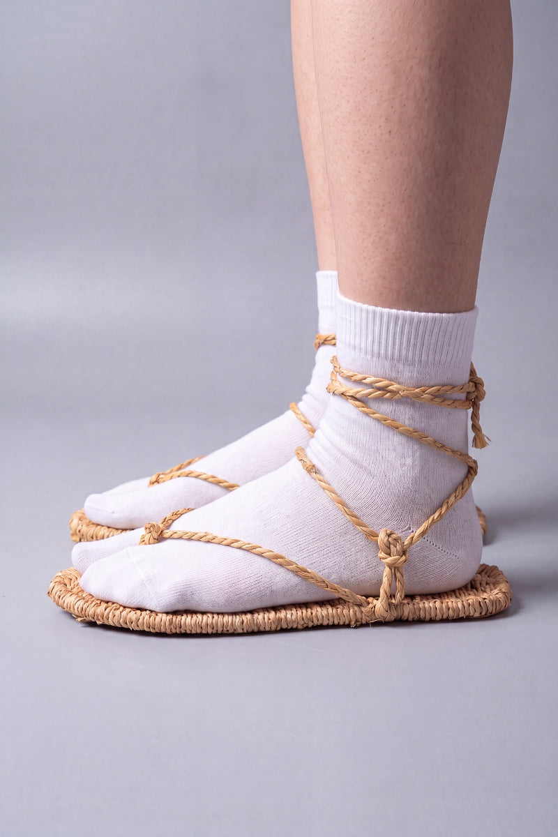 Side profile of waraji sandals worn with white tabi socks, showing the woven straw sole and ankle wrap